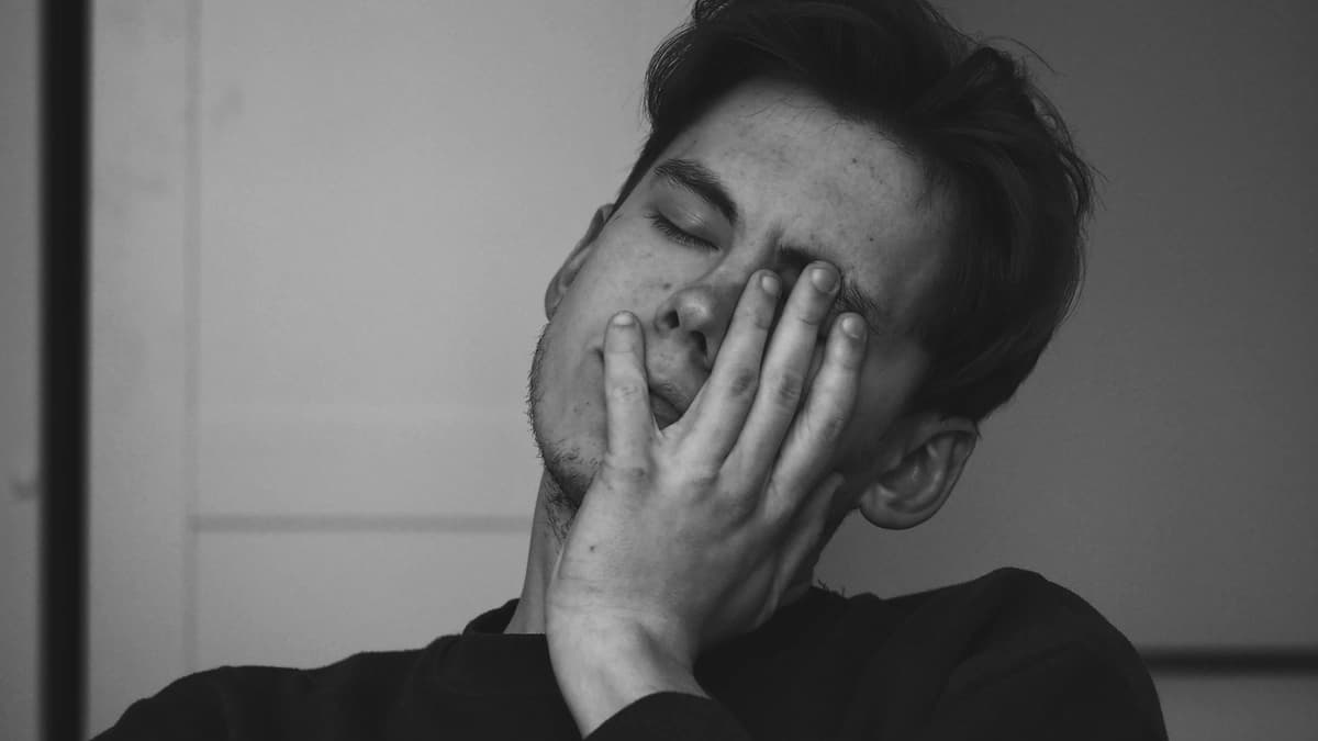 black and white portrait of young man with his head tilted, eyes closed, and left hand on his face in exasperation 