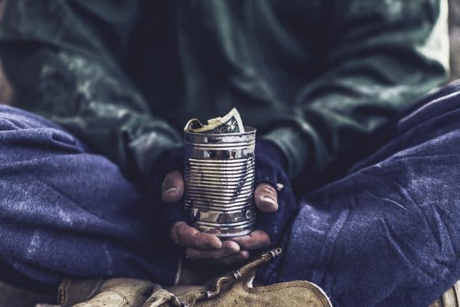 close up of homeless person holding a tin cup with money in it