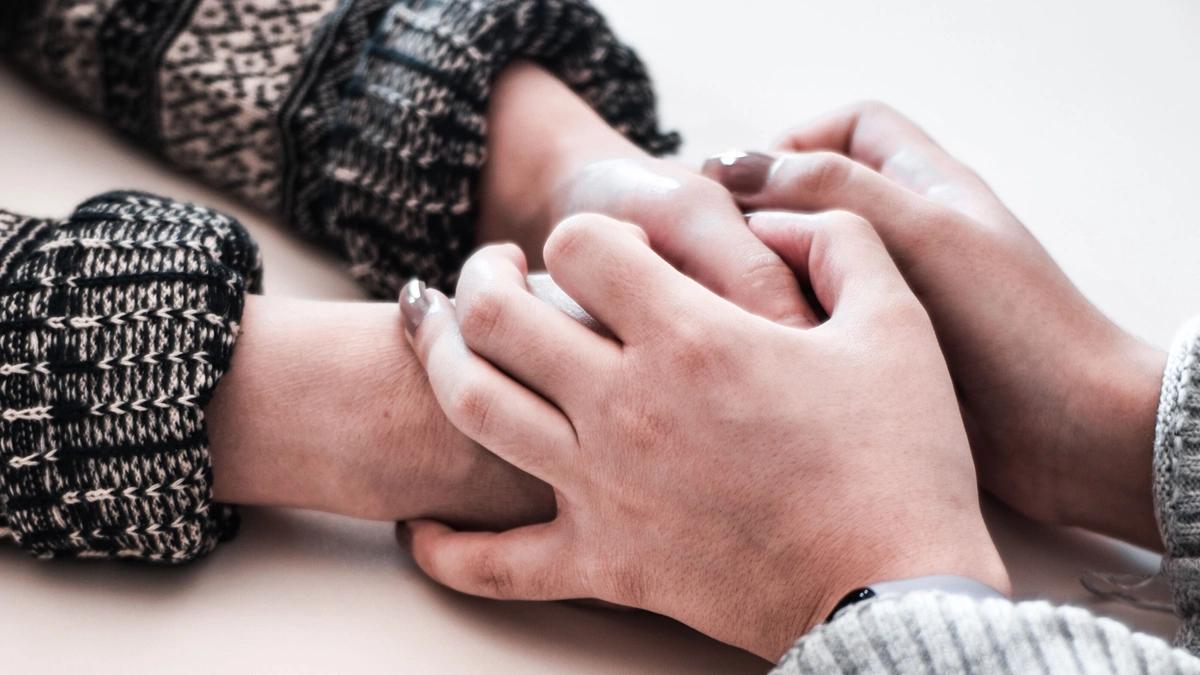 Two sets of hands holding one another on a table, close up of hands with sleeves of sweaters showing